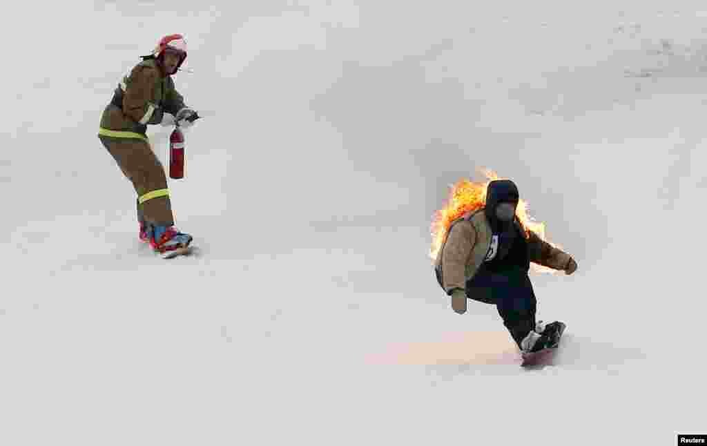 Snowboarders in fancy costumes, depicting a firefighter and fire victim, slide down before an attempt to cross a pool of water at the foot of a ski slope at the Bobrovy Log ski resort on the suburbs of the Siberian city of Krasnoyarsk, Russia.