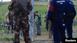FILE - A migrant child looks at Hungarian policemen and soldier in Roszke, Hungary, Sept. 15, 2015. Hungarian police detained 16 people claiming to be Syrian and Afghan migrants for illegally crossing the Serbian border fence, a police spokeswoman said.