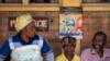 Patients waiting for prescriptions to be filled by the hospital pharmacy sit underneath a sign warning about the symptoms of Ebola, at Kibogora district hospital, near Lake Kivu and close to the border with Congo, in western Rwanda, Nov. 4, 2019.