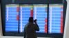 FILE - A man stands in front of a screen showing that multiple departure flights have been cancelled following the outbreak of the coronavirus, at an airport in Wuhan, Hubei province, China, Jan. 23, 2020. 