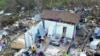 Two Haitian migrants sit as one stands amid the ruins of a home destroyed by Hurricane Dorian in Abaco, Bahamas, Sept. 28, 2019. 
