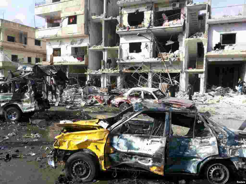 People inspect the site of a double bomb attack in the government-controlled city of Homs, Syria, in this handout picture provided by SANA.
