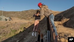 FILE - In this Jan. 3, 2019, file photo, a migrant from Honduras passes a child to her father after he jumped the border fence to get into the U.S. side to San Diego, Calif., from Tijuana, Mexico. The Trump administration says it would require extraordinary effort to reunite what