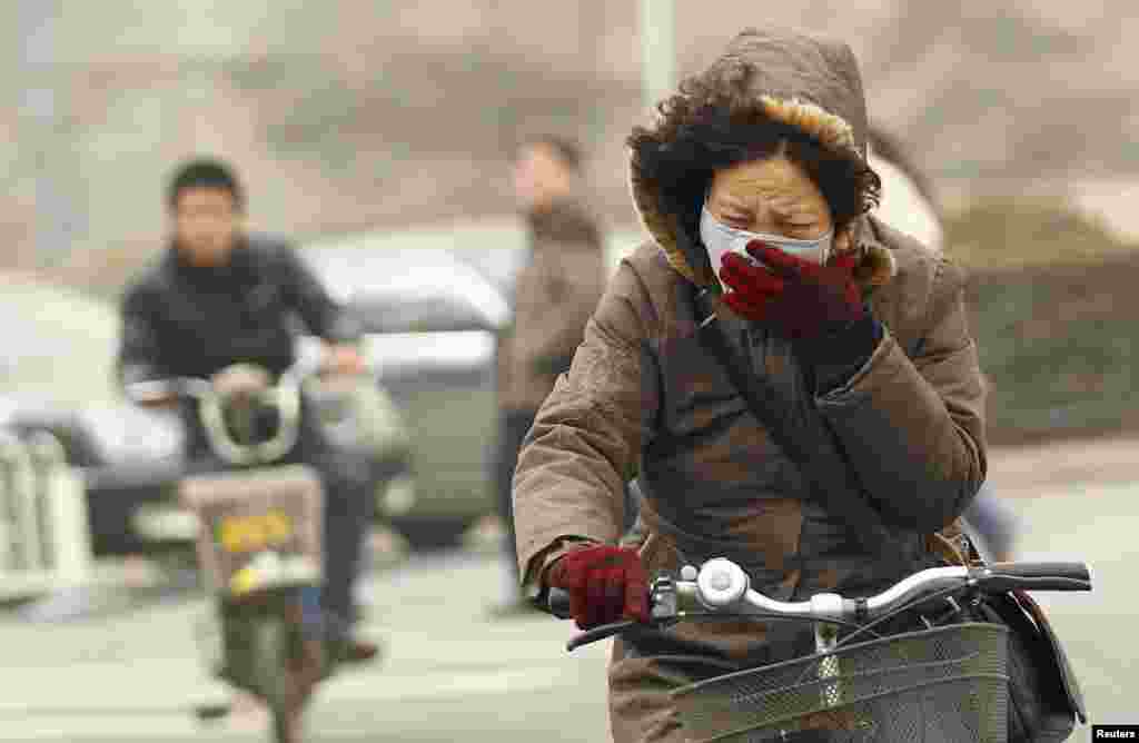 Seorang perempuan bersepeda sambil mengenakan masker di jalanan yang berkabut pada pagi hari di Beijing, Tiongkok.