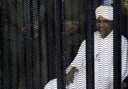 FILE - Sudan's former president Omar Hassan al-Bashir sits guarded inside a cage at the courthouse in Khartoum, Aug. 19, 2019.